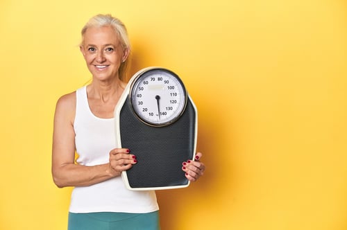 athletic-middleaged-woman-holding-scale-focused-fitness-yellow-studio