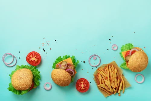 deliciosas-hamburguesas-ternera-tomate-queso-cebolla-pepino-lechuga-sobre-fondo-azul-vista-superior-espacio-copia-banner-comida-rapida-comida-llevar-concepto-dieta-poco-saludable (1)