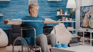 elder-person-with-disability-stretching-resistance-band-and-following-training-lesson-on-tablet-woman-sitting-in-wheelchair-pulling-elastic-belt-in-front-of-device-with-workout-video