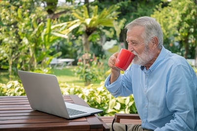 senior-man-executive-with-white-hair-using-computer-laptop-working-at-home-drinking-coffee-looking-camera